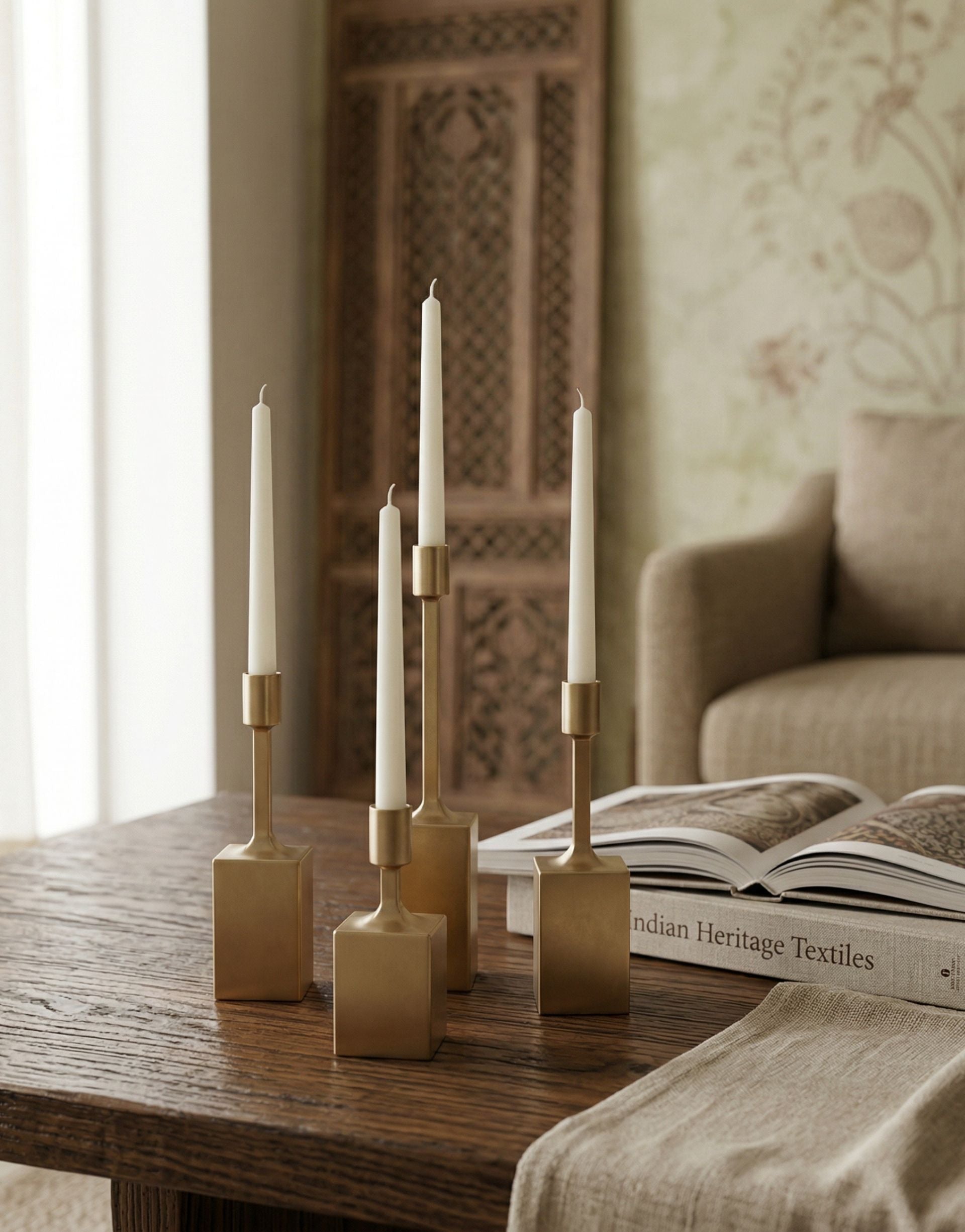 Decorative brass candles on a wooden table with a book and sofa in the background