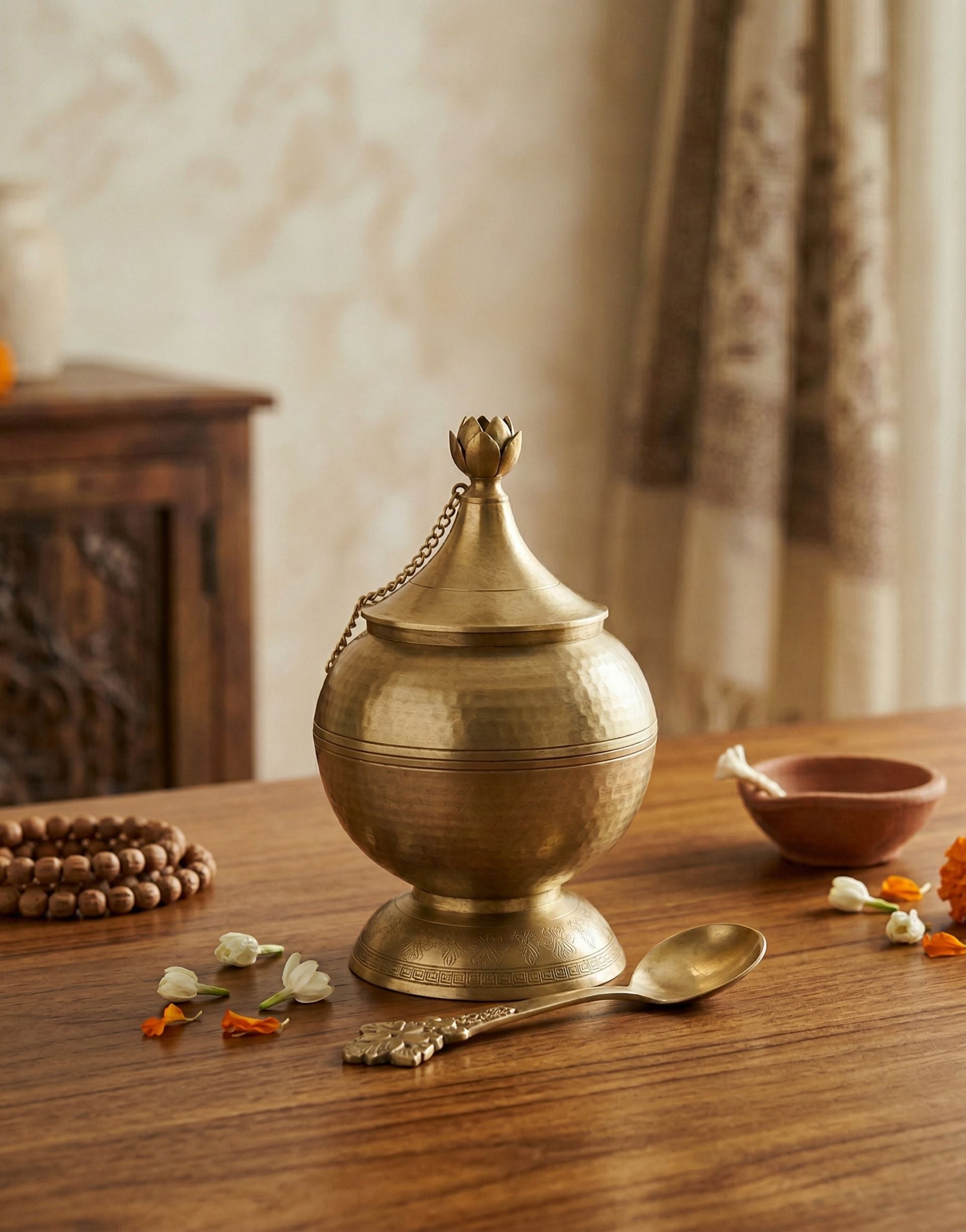 Brass ghee container with a chain on a wooden table with decorative elements.