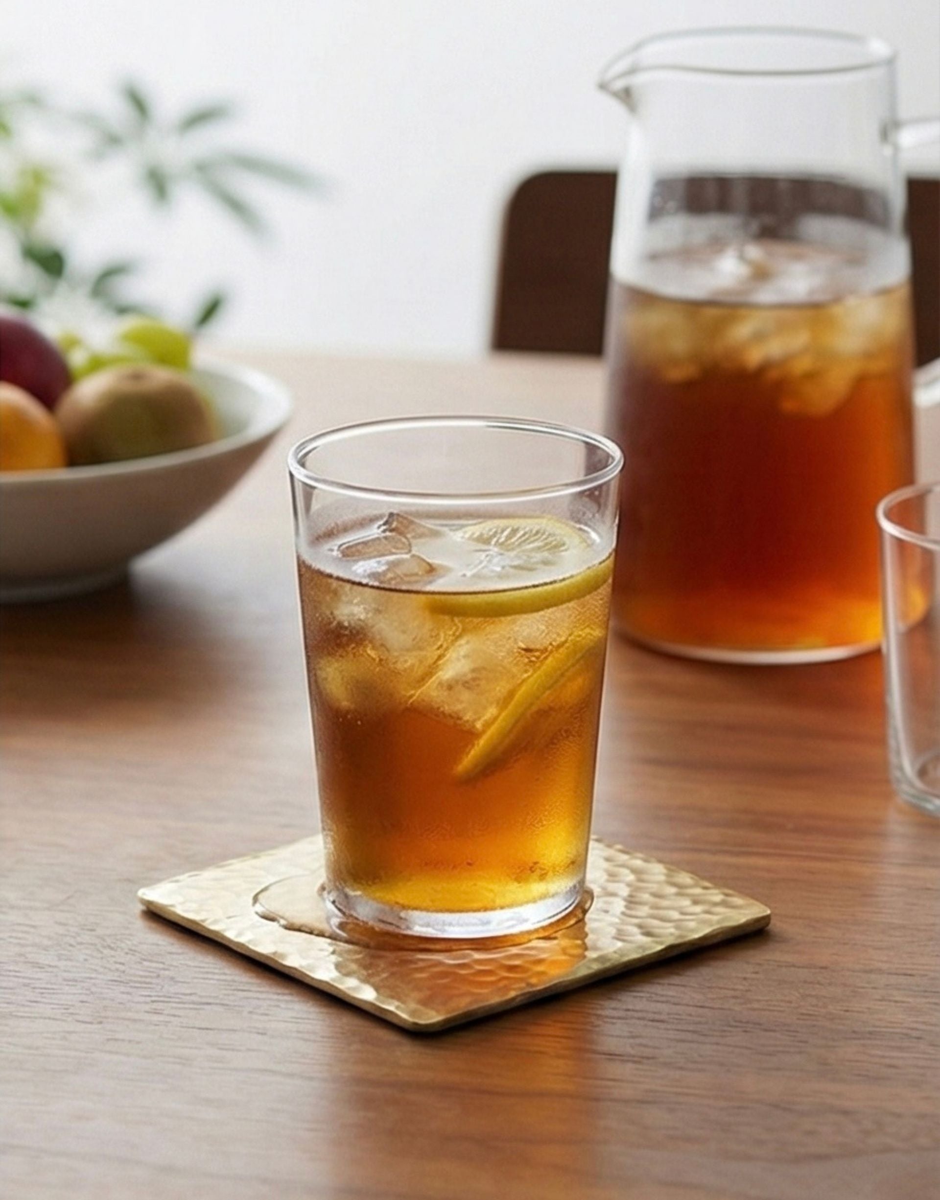 Glass of iced tea with a pitcher on a brass coaster on a wooden table