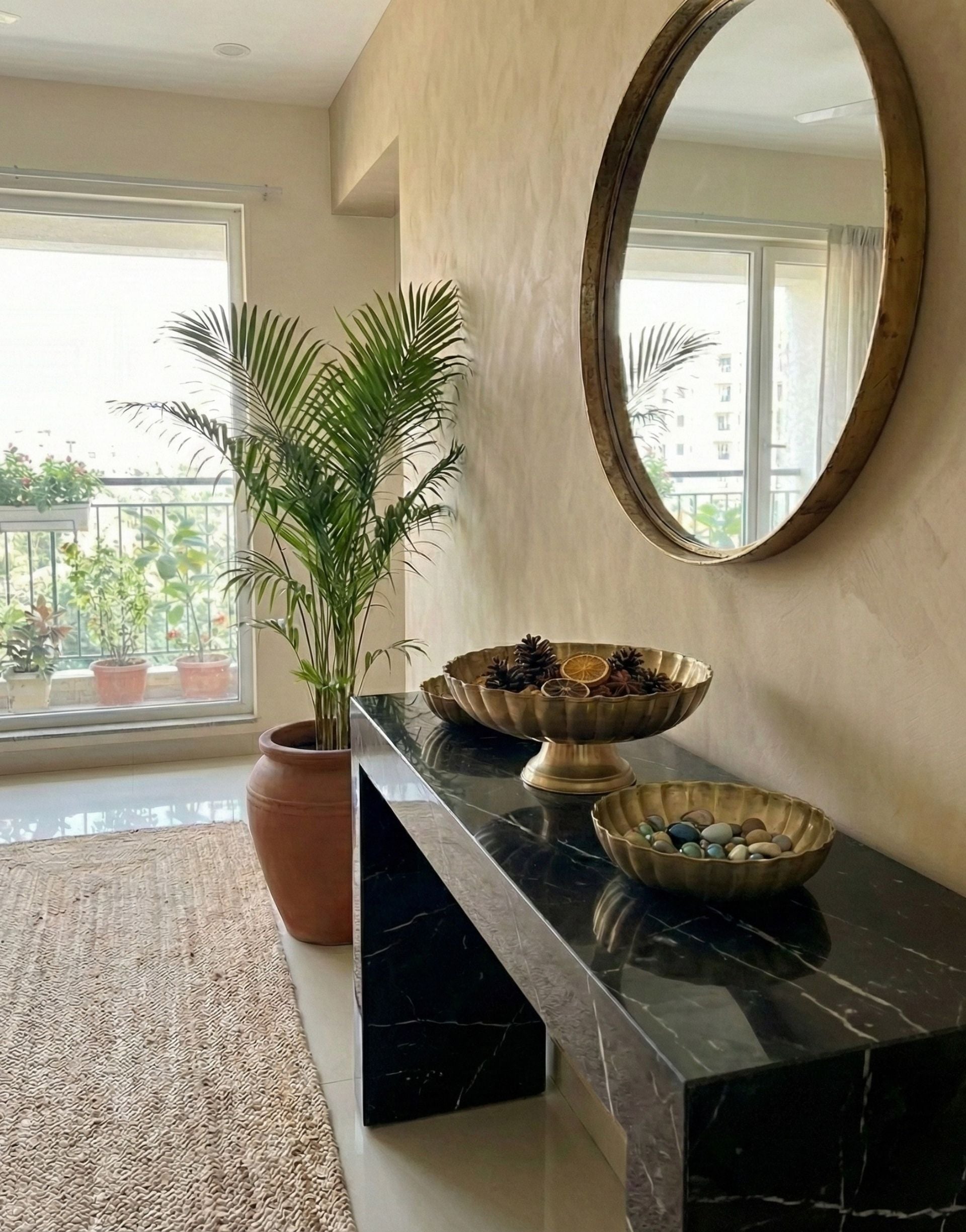 Decorative setup with a plant, brass bowls, and a mirror on a marble surface.