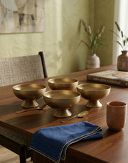 Set of brass desert bowls on a wooden table with a blue napkin and a brown mug.