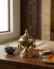 Brass incense burner on a wooden surface with a bowl of incense sticks and a small dish.