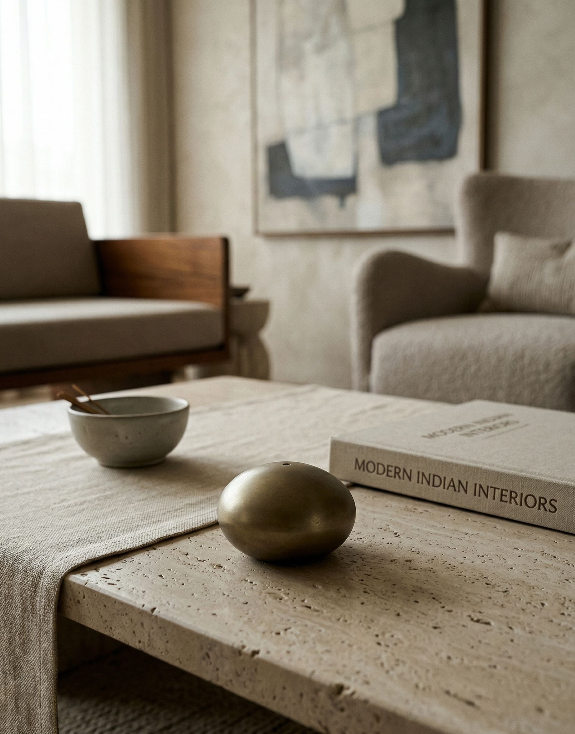 Table with brass incense holder and a book titled 'Modern Indian Interiors' in a living room setting.