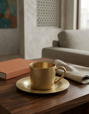 Brass tea cup and saucer on a wooden table with a blurred living room background