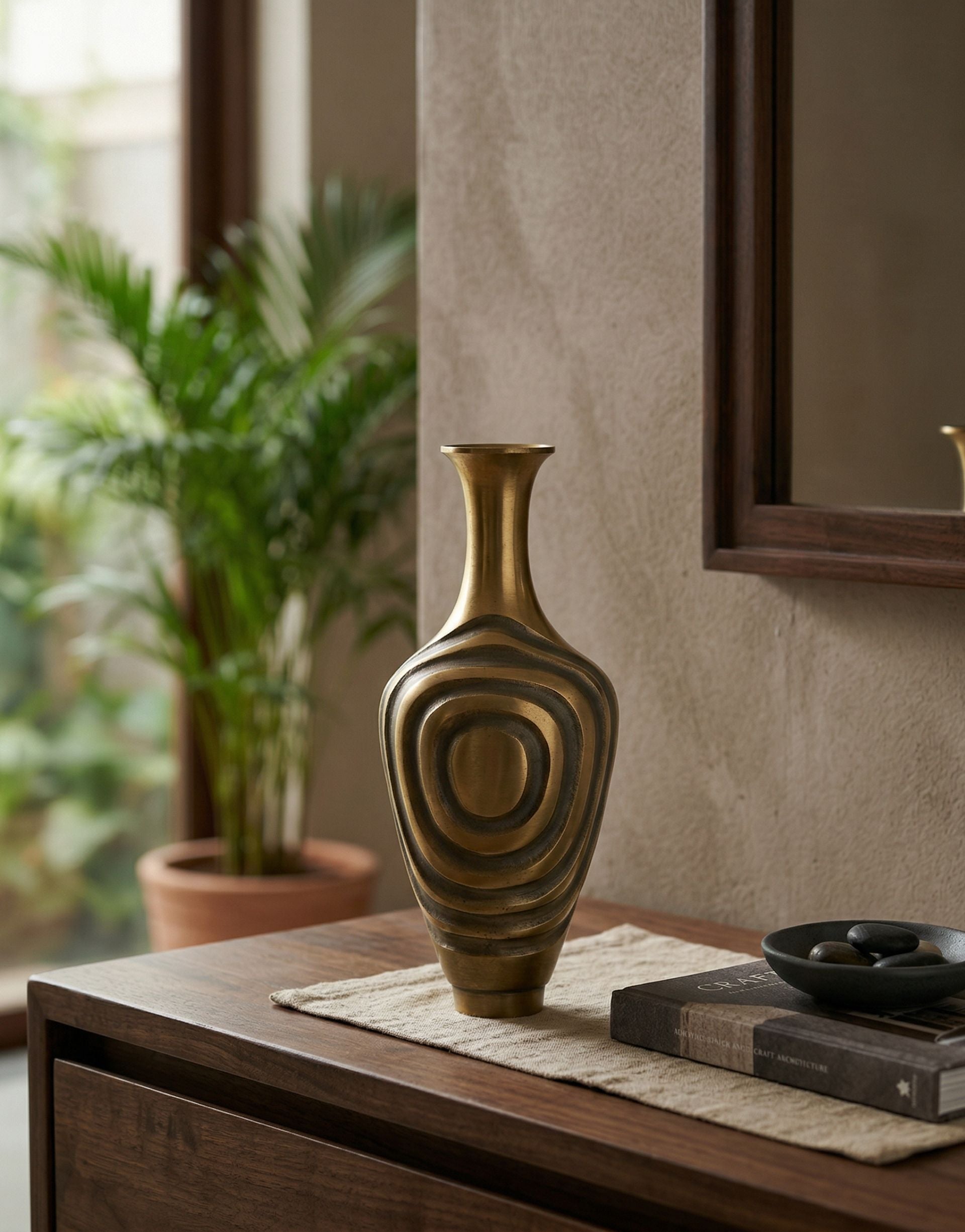 Decorative brass vase on a wooden surface with a plant and mirror in the background