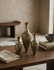 Three brass vases on a wooden table with a neutral background