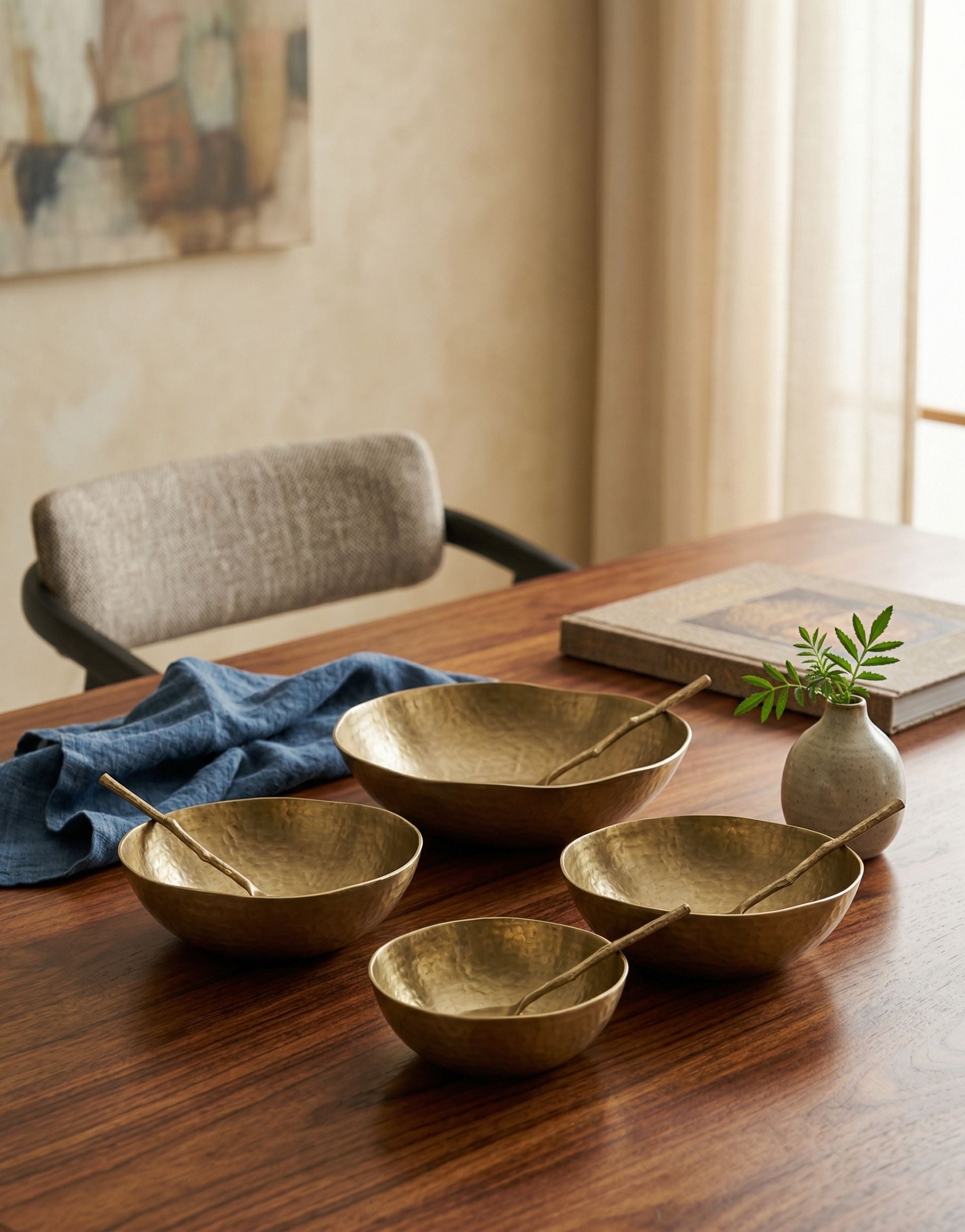 Set of brass dinner serving bowls on a wooden table with a chair and decor in the background