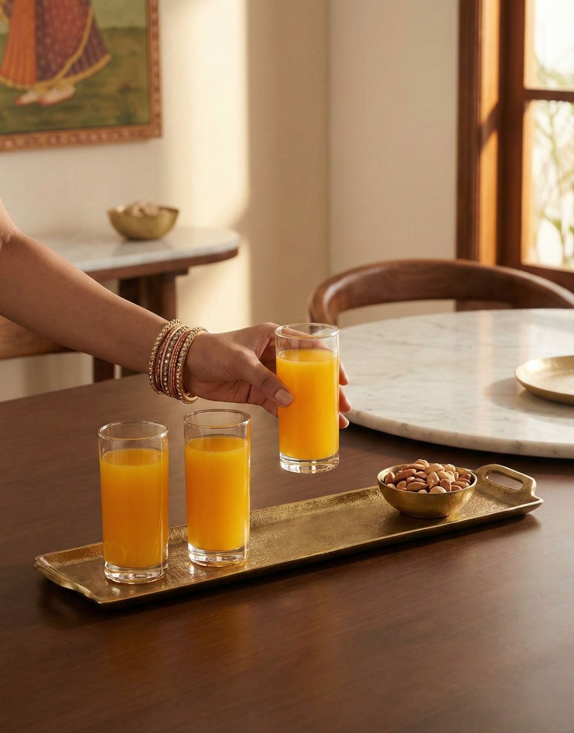 Person serving glasses of orange juice on a wooden table with a brass tray.