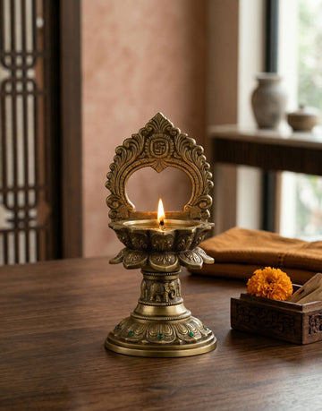 Decorative brass diya with a lit candle on a wooden surface