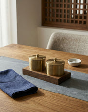 Two brass salt and pepper containers on a wooden tray with a blue napkin on a wooden table.