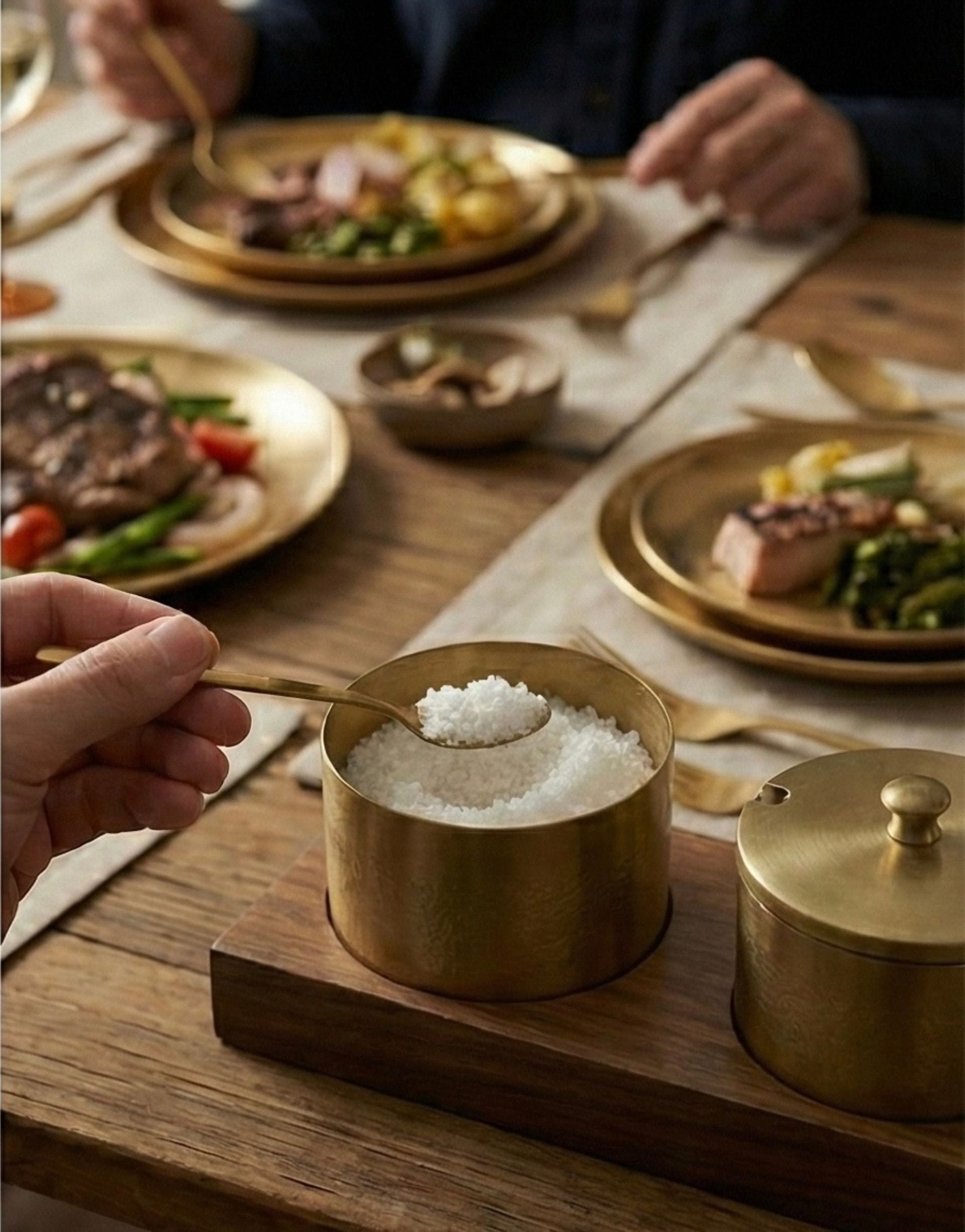 Brass salt cellar on a wooden tray with a table setting in the background