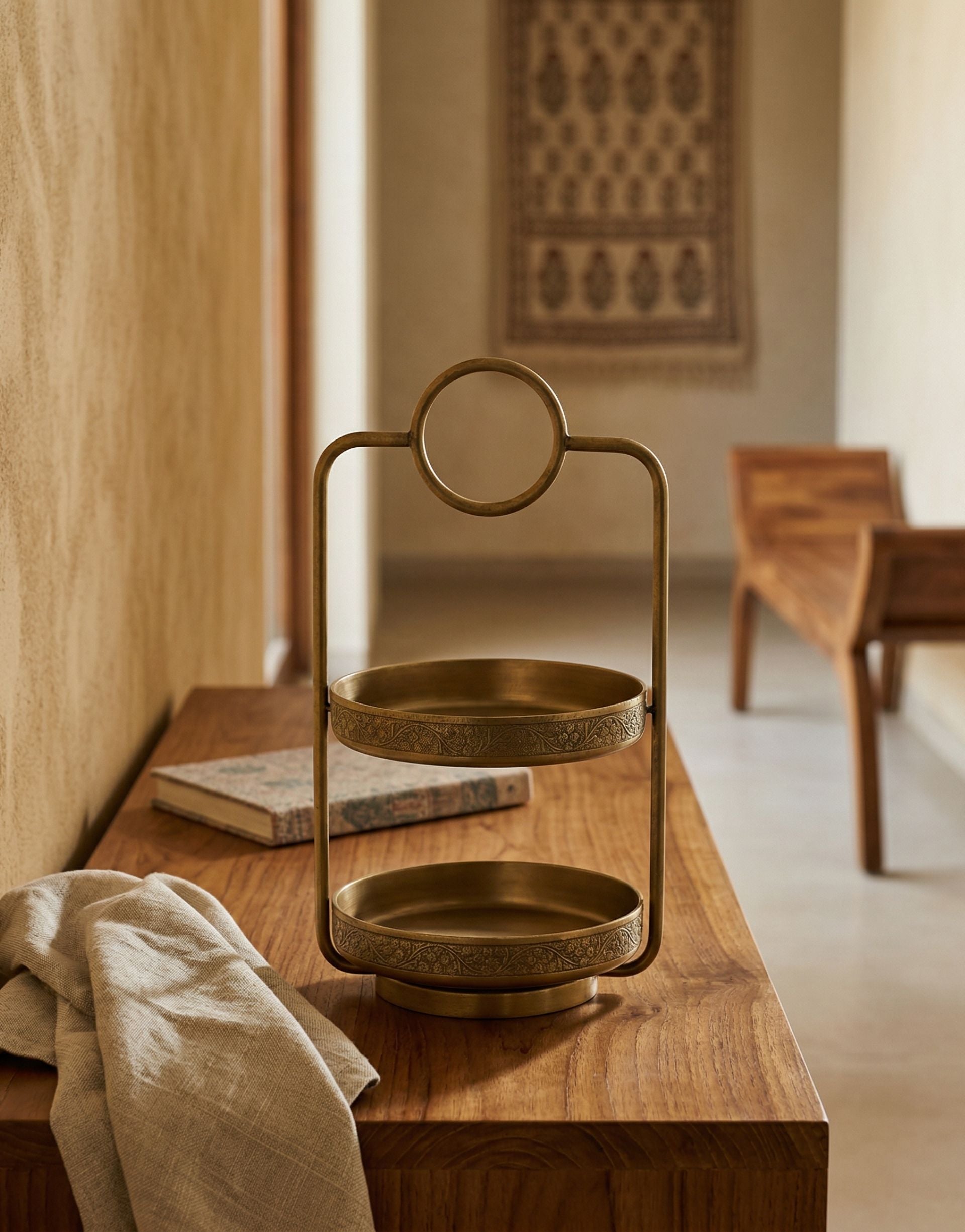 Brass two-tiered tray on a wooden surface with a blurred room background