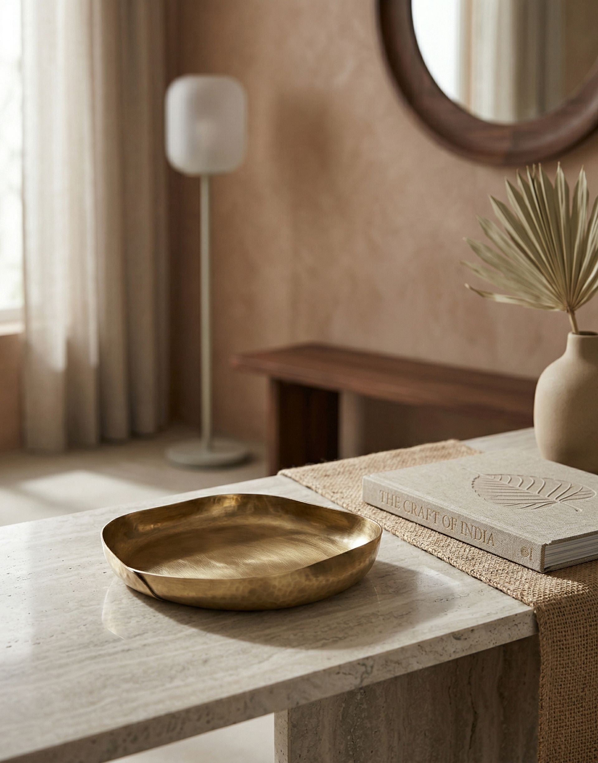 Brass trinket tray on a table with a lamp and mirror in the background