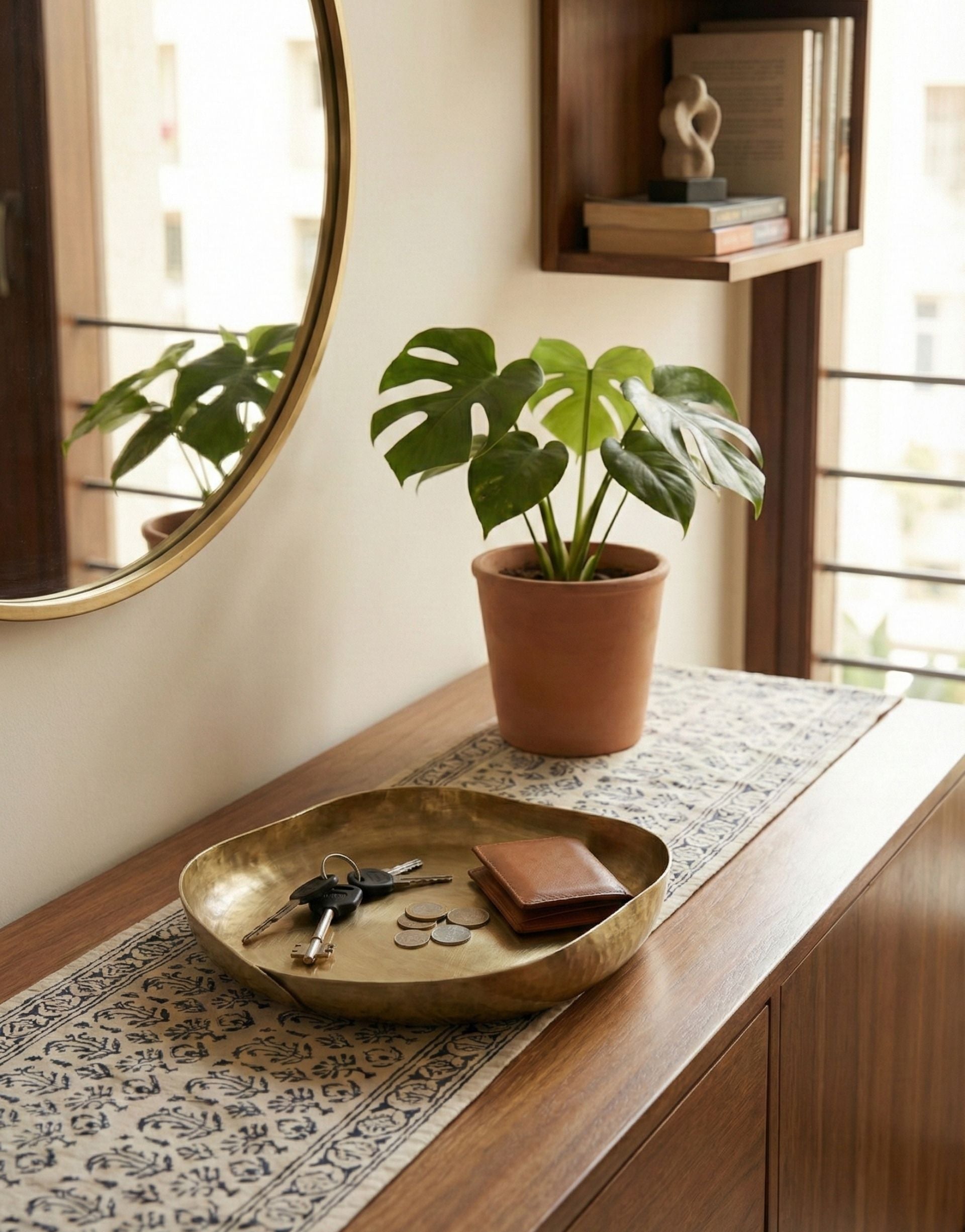 Brass trinket tray with potted plant on a wooden surface with a mirror and books in the background