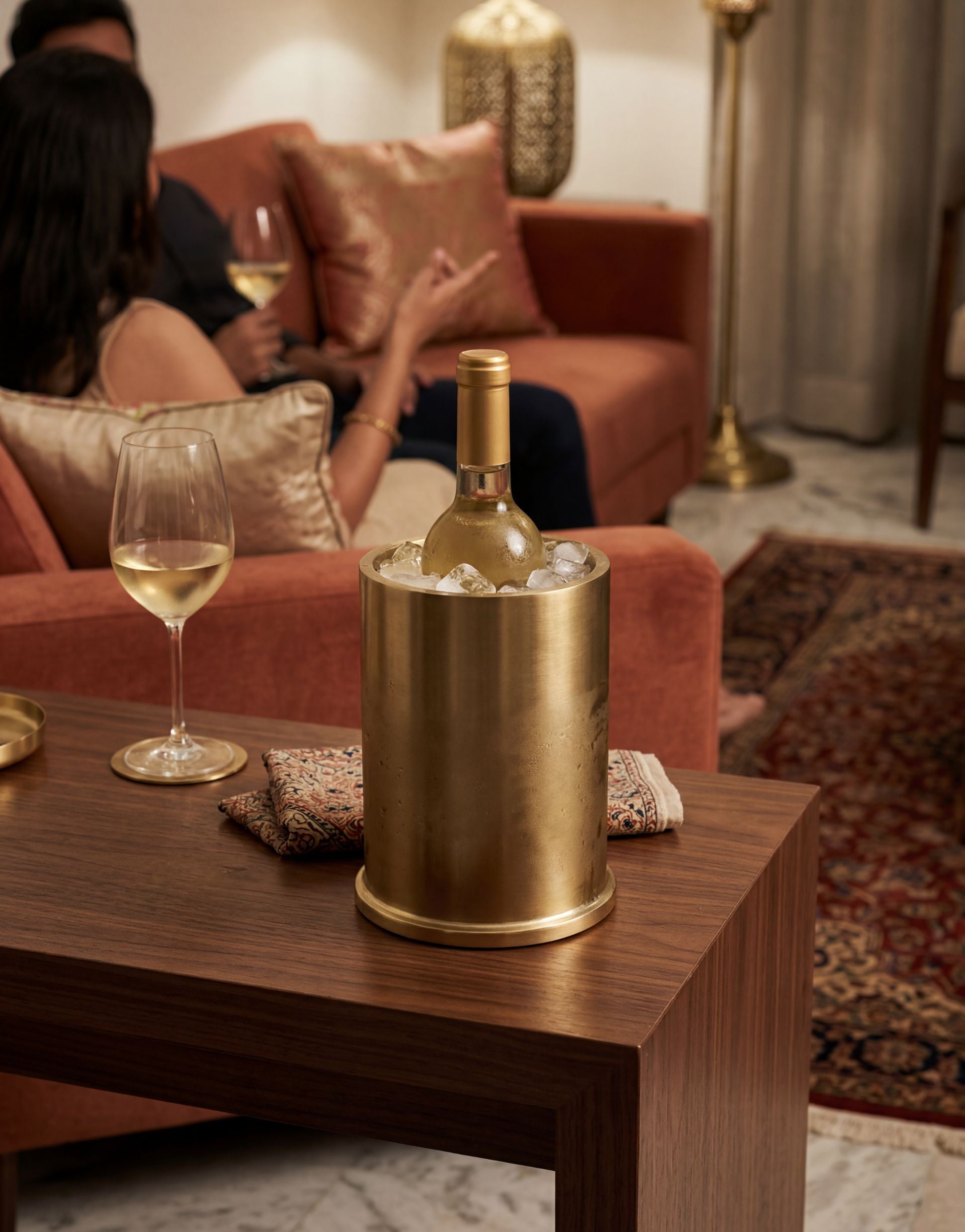 Brass wine cooler with a bottle of white wine on a table with people enjoying a meal.